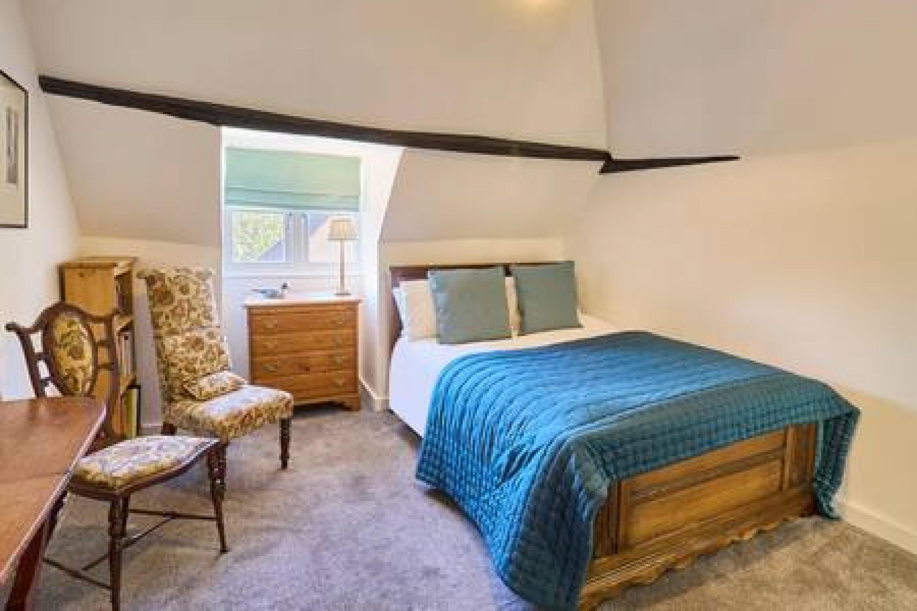 A bedroom with a bed, a chair, a dresser, and a window.