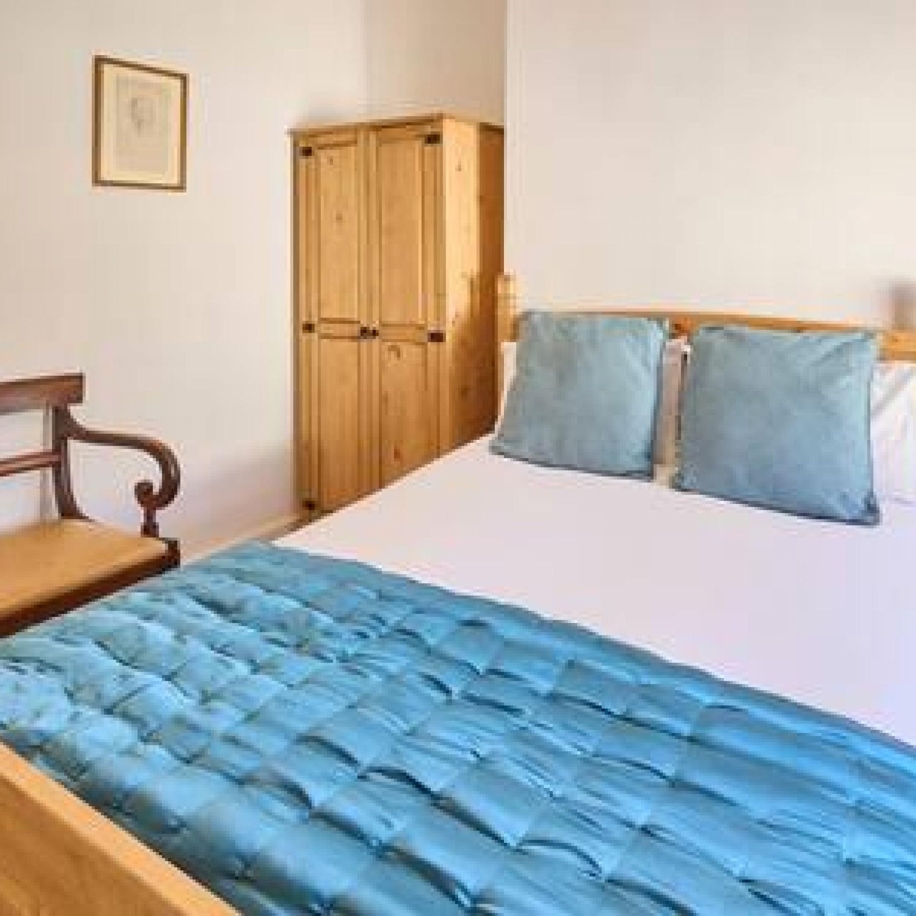 A bedroom with a bed, wooden wardrobe, and a framed picture on the wall.