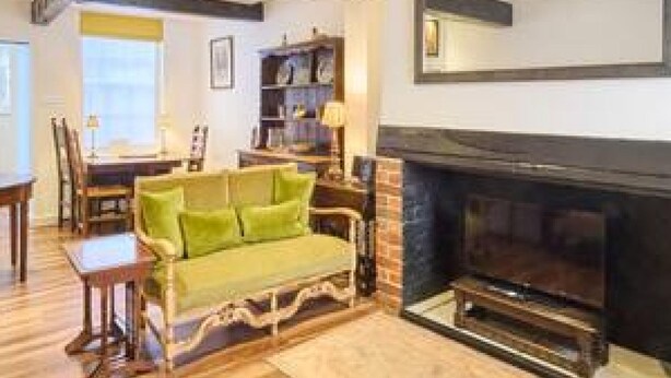 A living room with a green sofa, wooden flooring, a fireplace, and a large mirror above it. - Host Stay St Radigunds House (Canterbury)