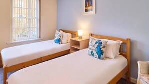A room with two single beds, a nightstand with a lamp, a chair, and a window with bars. - Host Stay Cobb Court (Margate)