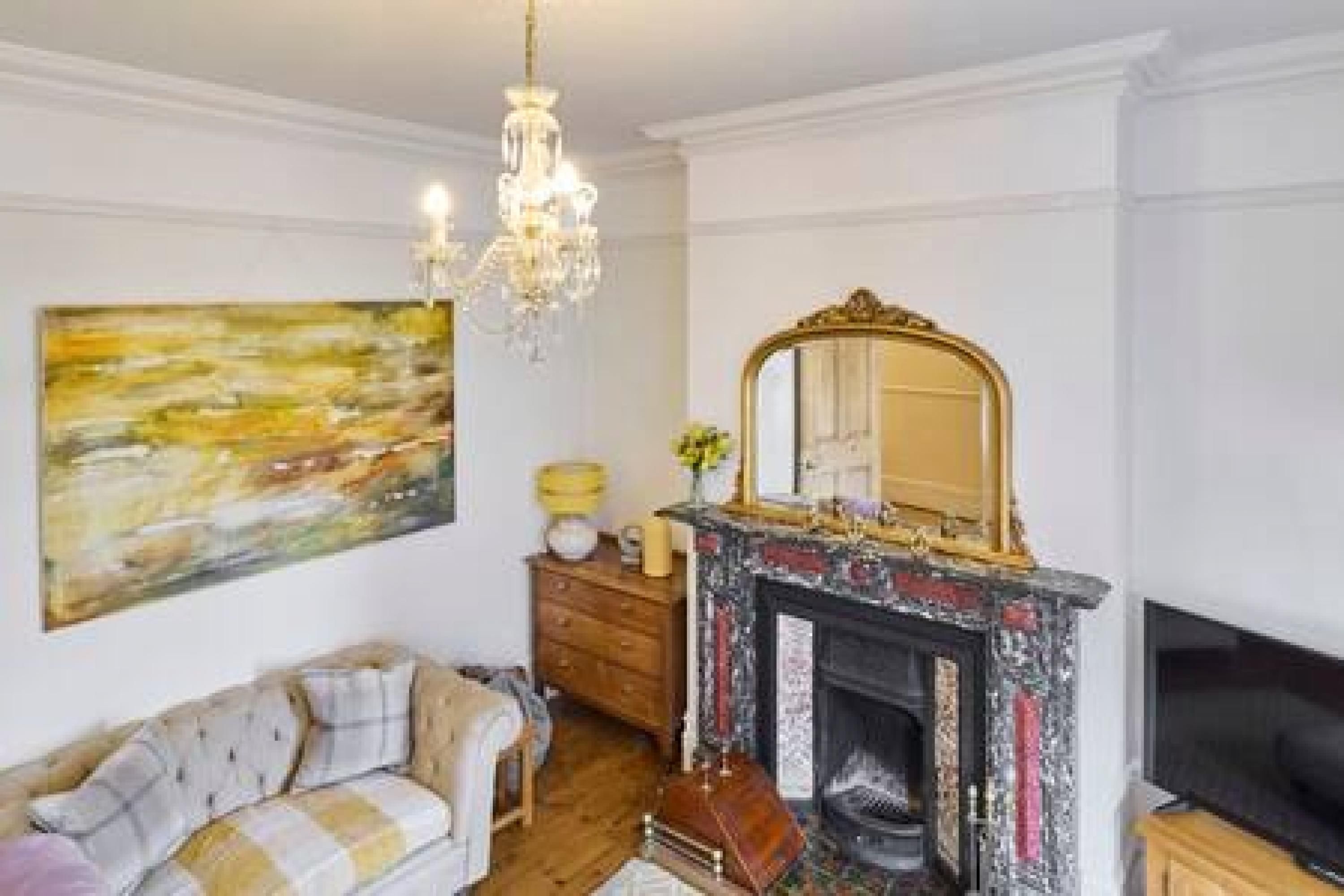 A living room with a fireplace, a sofa, a television, and a chandelier.