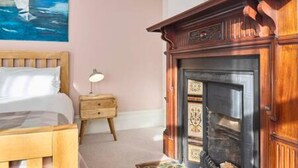 A bedroom with a wooden bed, a nightstand, a fireplace, and a painting on the wall. - Host Stay Bellevue Road (Ramsgate)