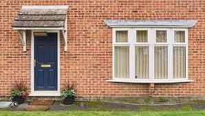 A two-story brick house with a front door, a bay window, and a small porch area with potted plants. - Host Stay Mayfield (Canterbury)