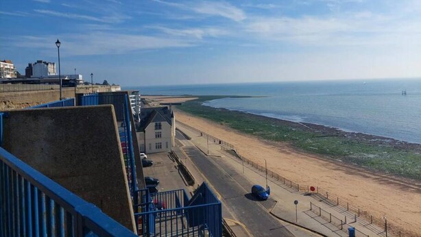 Ein Küstenblick mit Strand, Promenade und Gebäuden im Hintergrund.