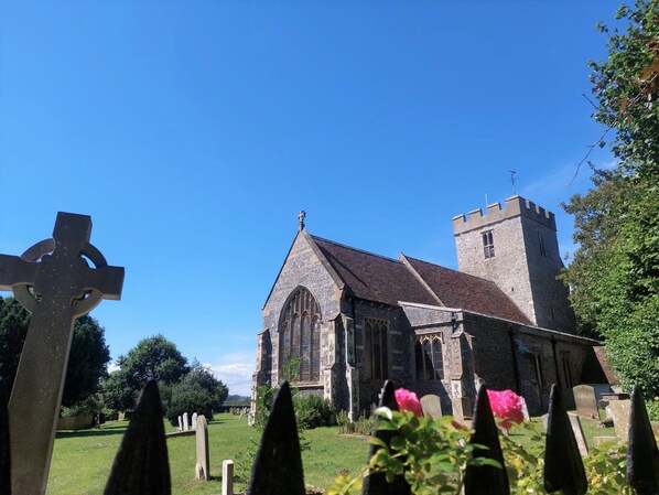 A church with a tall tower and a stone facade, surrounded by a cemetery with headstones and a cross in the foreground.