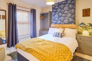 A hotel room with a bed, a bedside table, a nightstand, a window with curtains, and a wall with a nautical-themed wallpaper. - Host Stay Ethelbert Cottage (Broadstairs)