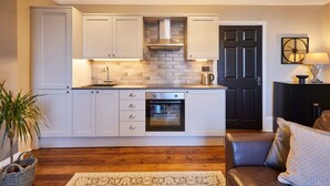 A compact kitchen with white cabinets, a built-in oven, and a black door. - Host Stay Endeavour Sails (Whitby)
