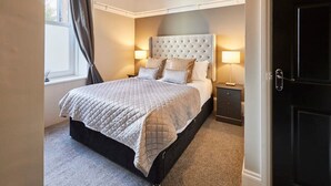 A bedroom with a large bed, two bedside tables, a dark door, and a window with curtains. - Host Stay Endeavour Sails (Whitby)