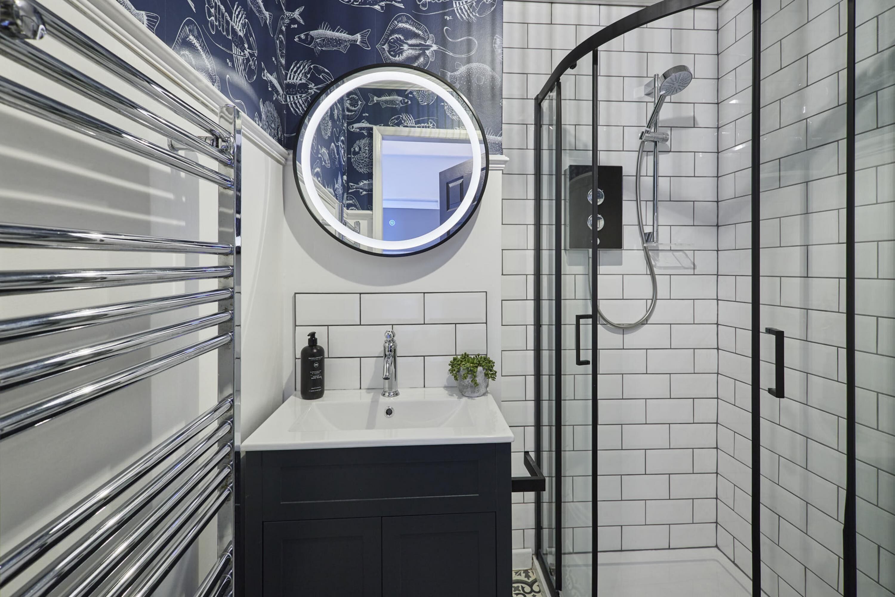 A modern bathroom with a white sink, black vanity, a round mirror, and a glass-enclosed shower.