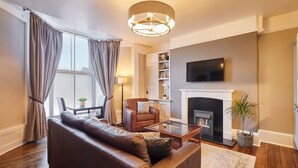 A living room with a sofa, armchair, coffee table, fireplace, television, and a bookshelf. - Host Stay Endeavour Sails (Whitby)