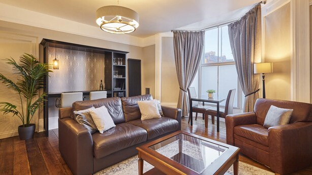 A modern living room with leather sofas, a glass coffee table, and a dining area with a table and chairs. - Host Stay Endeavour Sails (Whitby)