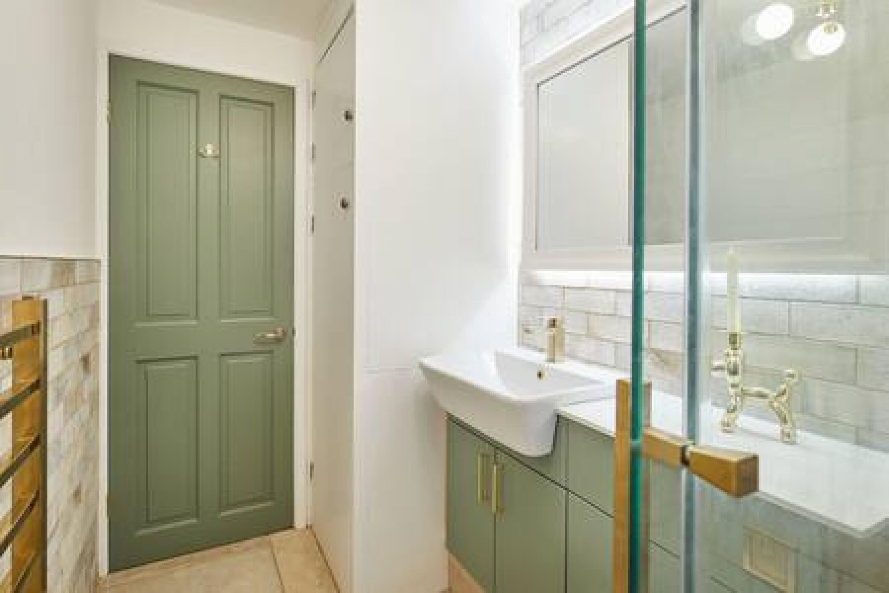 Un baño con puerta verde, lavabo blanco y cabina de ducha de cristal.