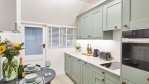 Een keuken met lichtgroene kastjes, een wit aanrechtblad en een eethoek met een tafel gedekt voor twee personen.