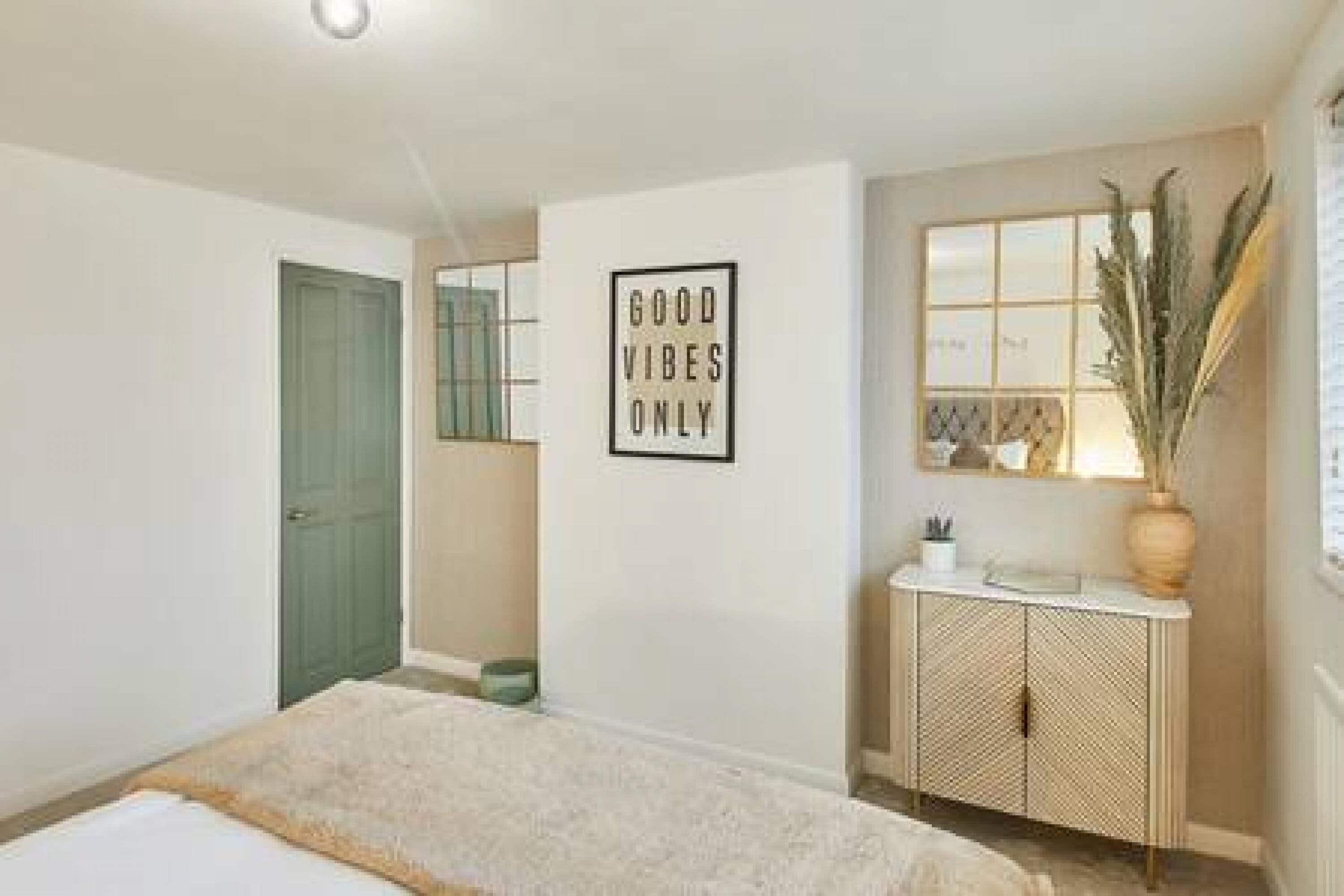 A bedroom with a bed, a bedside table, a mirror, and a wall with a 'Good Vibes Only' sign.