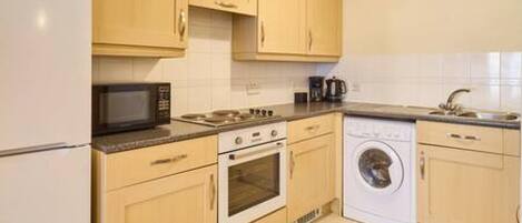 A compact kitchen with a refrigerator, microwave, stove, oven, and washing machine.