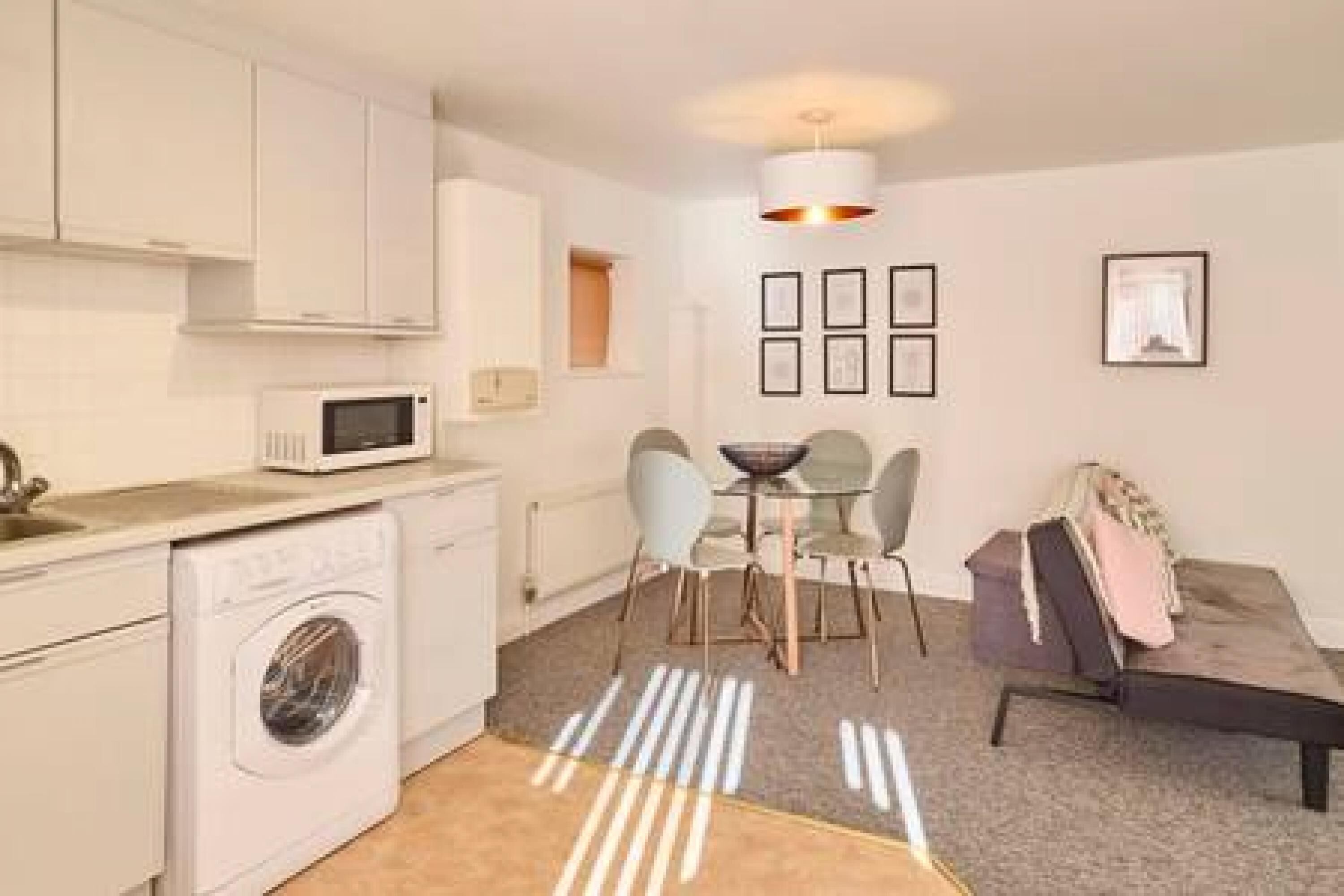 A compact kitchen with a washing machine, a microwave, and a dining area with chairs and a table.