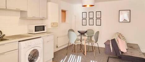 A compact kitchen with a washing machine, a microwave, and a dining area with chairs and a table.