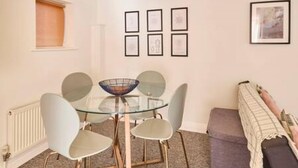 A dining area with a glass table, four chairs, and framed pictures on the wall. - Host Stay King s Corner (Canterbury)