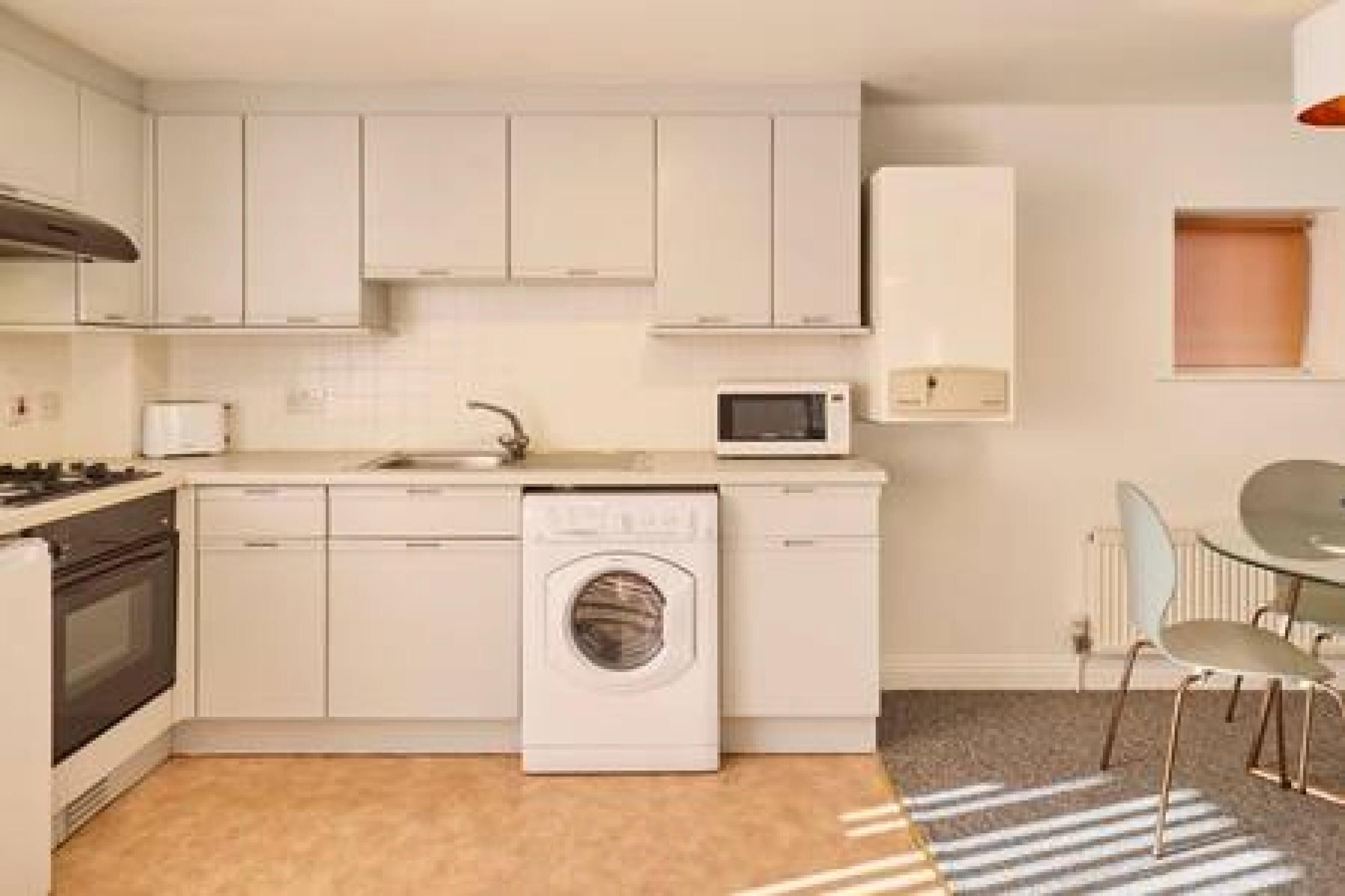 A compact kitchen with white cabinets, a microwave, a washing machine, and a small dining area with a table and chairs.
