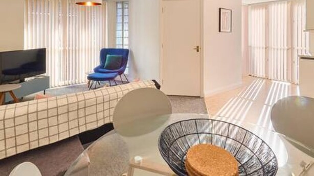 A modern living room with a sofa, a television, a glass coffee table, and a chair. - Host Stay King s Corner (Canterbury)