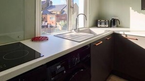 Une cuisine compacte équipée d’un lave-vaisselle intégré, d’un évier et d’une fenêtre donnant sur un quartier résidentiel.