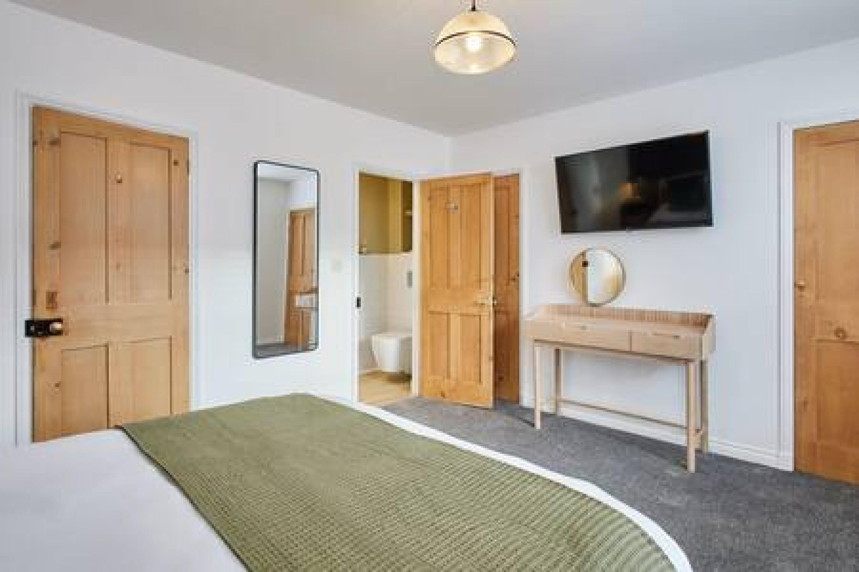 A bedroom with a bed, a bedside table, a mirror, and a TV mounted on the wall.