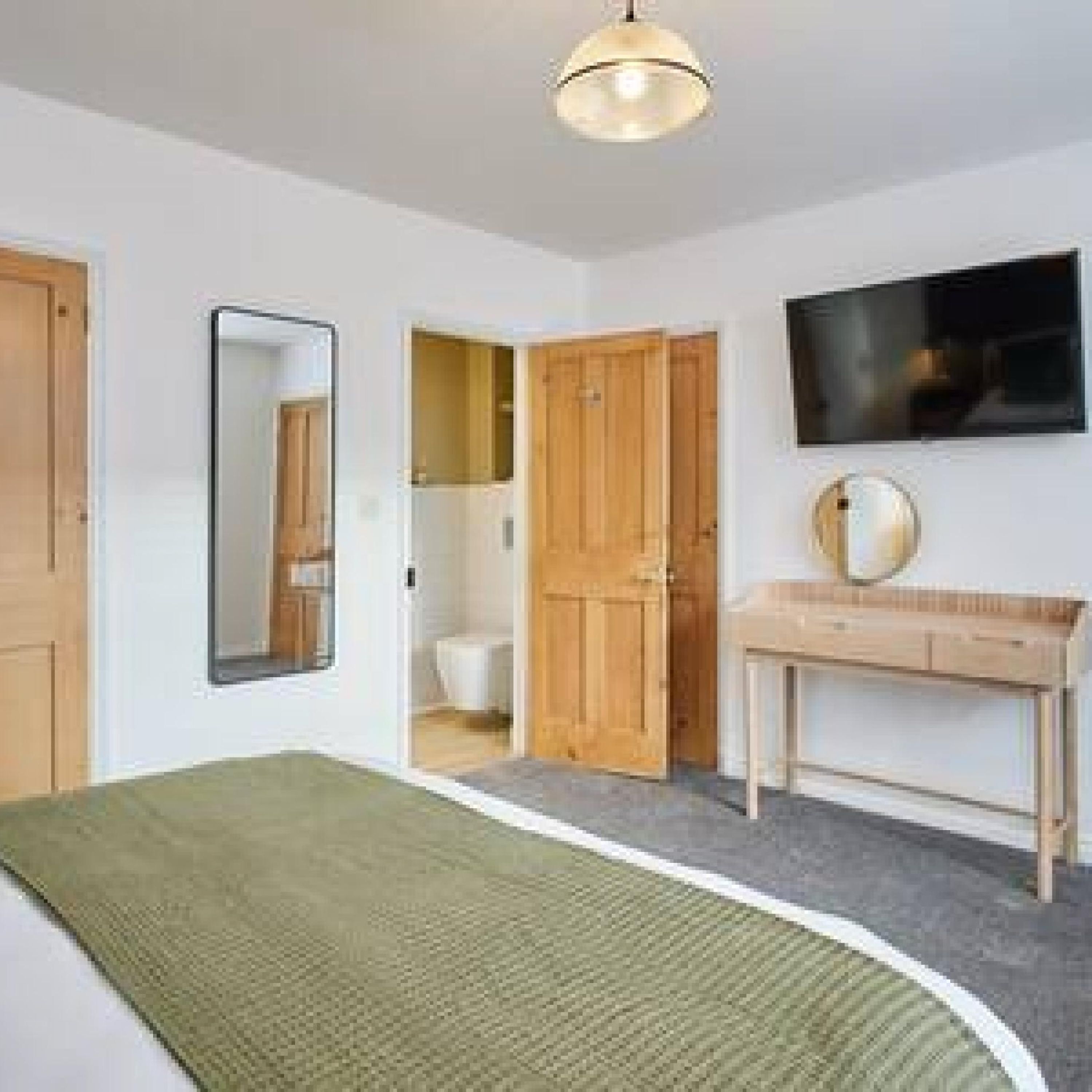 Een slaapkamer met een bed, een spiegel, een televisie en een houten garderobe.