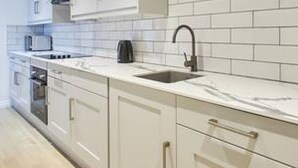A modern kitchen with white cabinetry, a black faucet, and a tiled backsplash. - Host Stay Penny Farthing Cottage (Whitby)