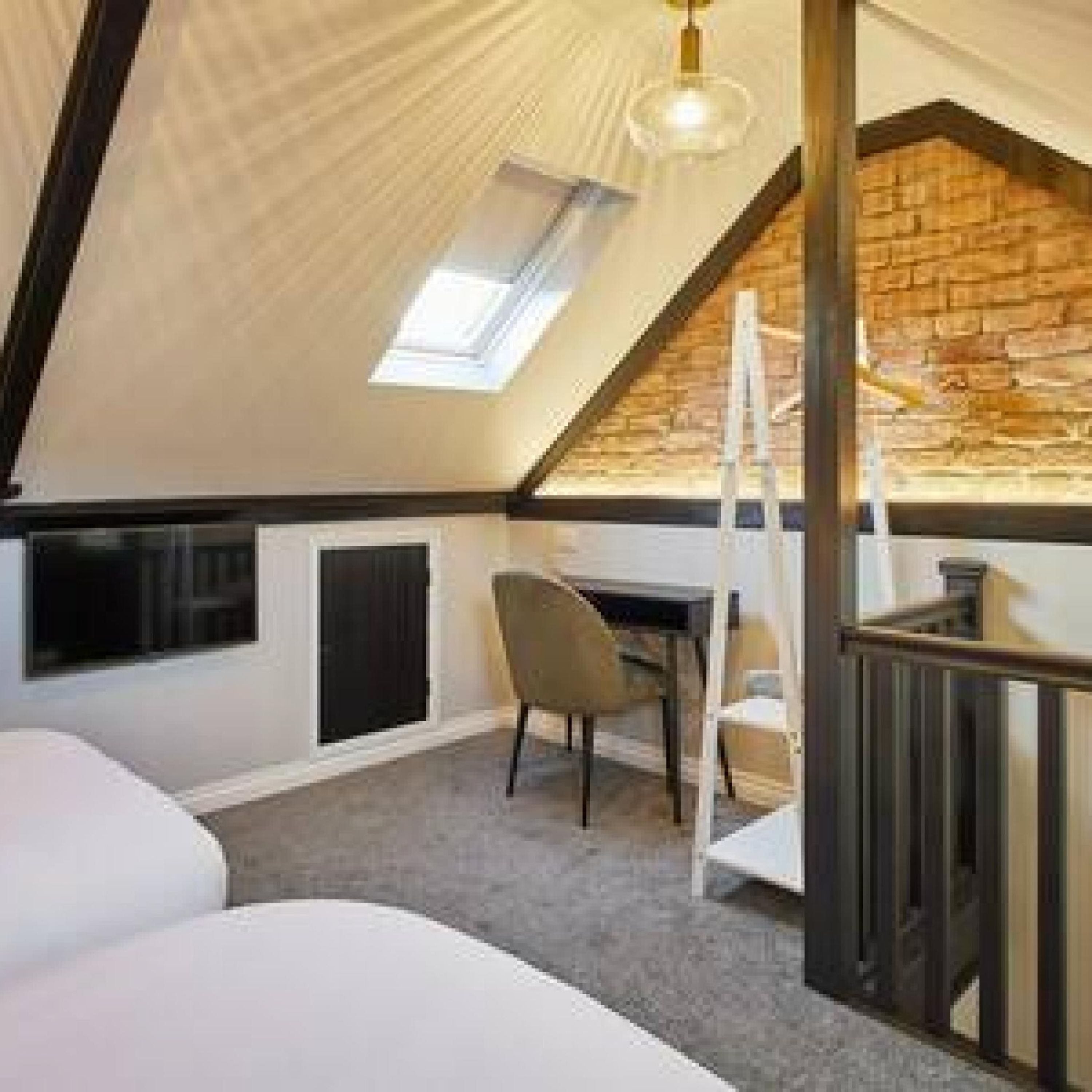 Ein Schlafzimmer im Loft-Stil mit schrägem Dach, einem Dachfenster, einem Schreibtisch und einem Sessel.