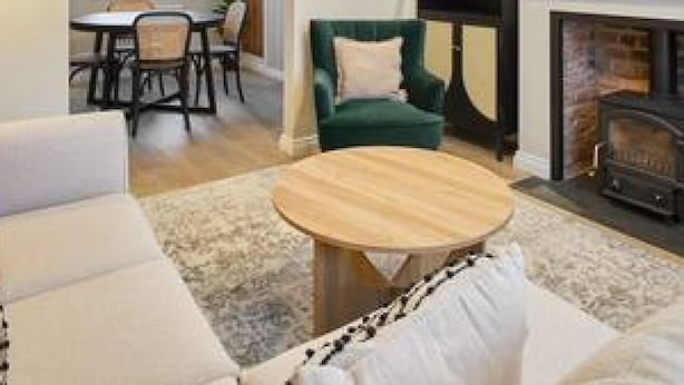 A modern living room with a sofa, a coffee table, and a fireplace. There is a dining area with chairs and a table visible through an open doorway. - Host Stay Penny Farthing Cottage (Whitby)