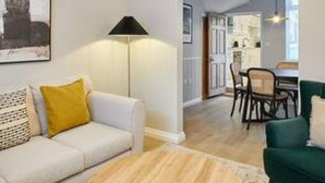 A living room with a sofa, a round coffee table, and a dining area with chairs and a table. - Host Stay Penny Farthing Cottage (Whitby)
