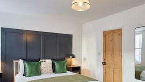 A bedroom with a bed, a nightstand, a lamp, and a door. - Host Stay Penny Farthing Cottage (Whitby)