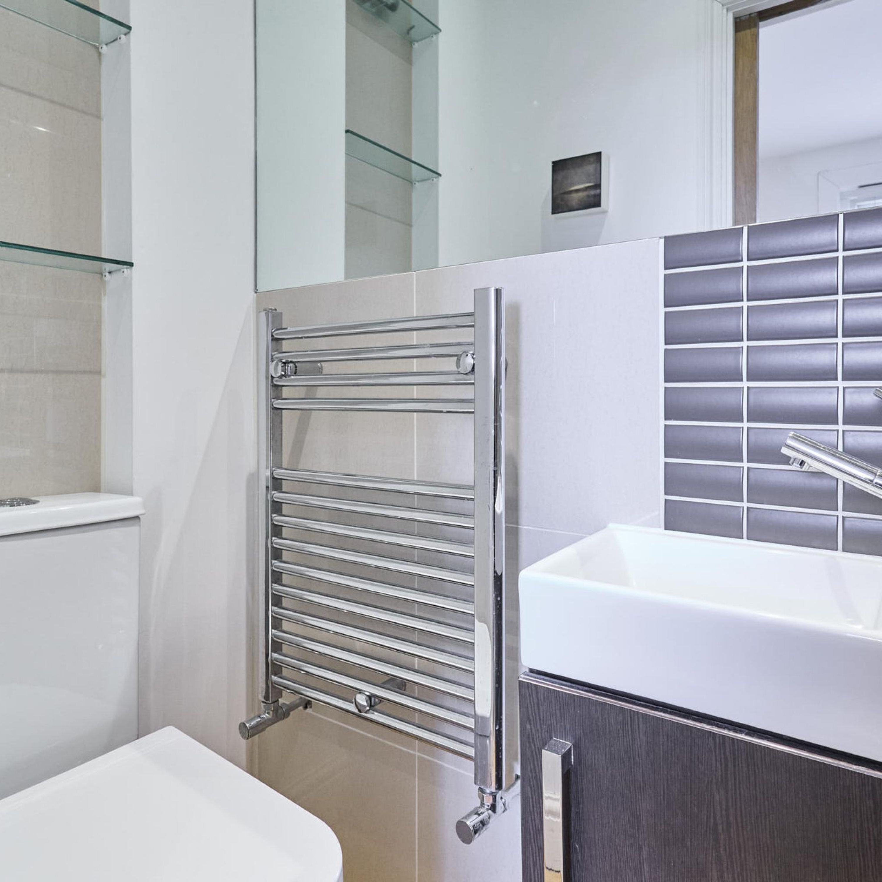 A modern bathroom with a glass shower enclosure, a chrome towel rack, a white sink, and a dark-toned cabinet.