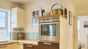 A modern kitchen with wooden cabinets, a built-in oven, and a backsplash. - Host Stay Sail Away (Whitstable)