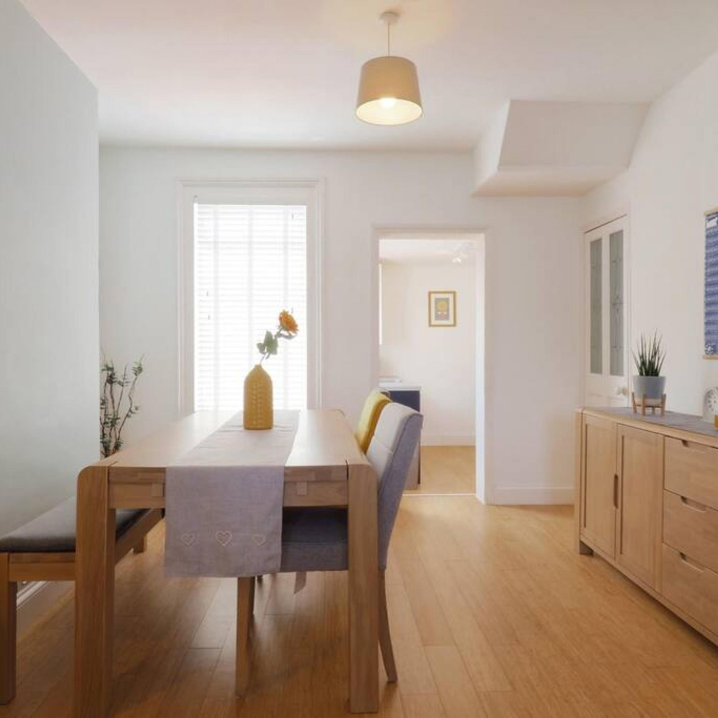 A modern, well-lit dining area with a wooden table, chairs, and a hanging light fixture.