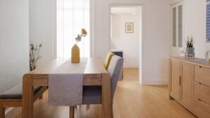 A modern, well-lit dining area with a wooden table, chairs, and a hanging light fixture. - Host Stay Herbert Road (Ramsgate)