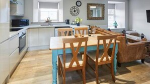 Une cuisine moderne avec des meubles blancs, une table à manger en bois et un mur d’accent bleu.