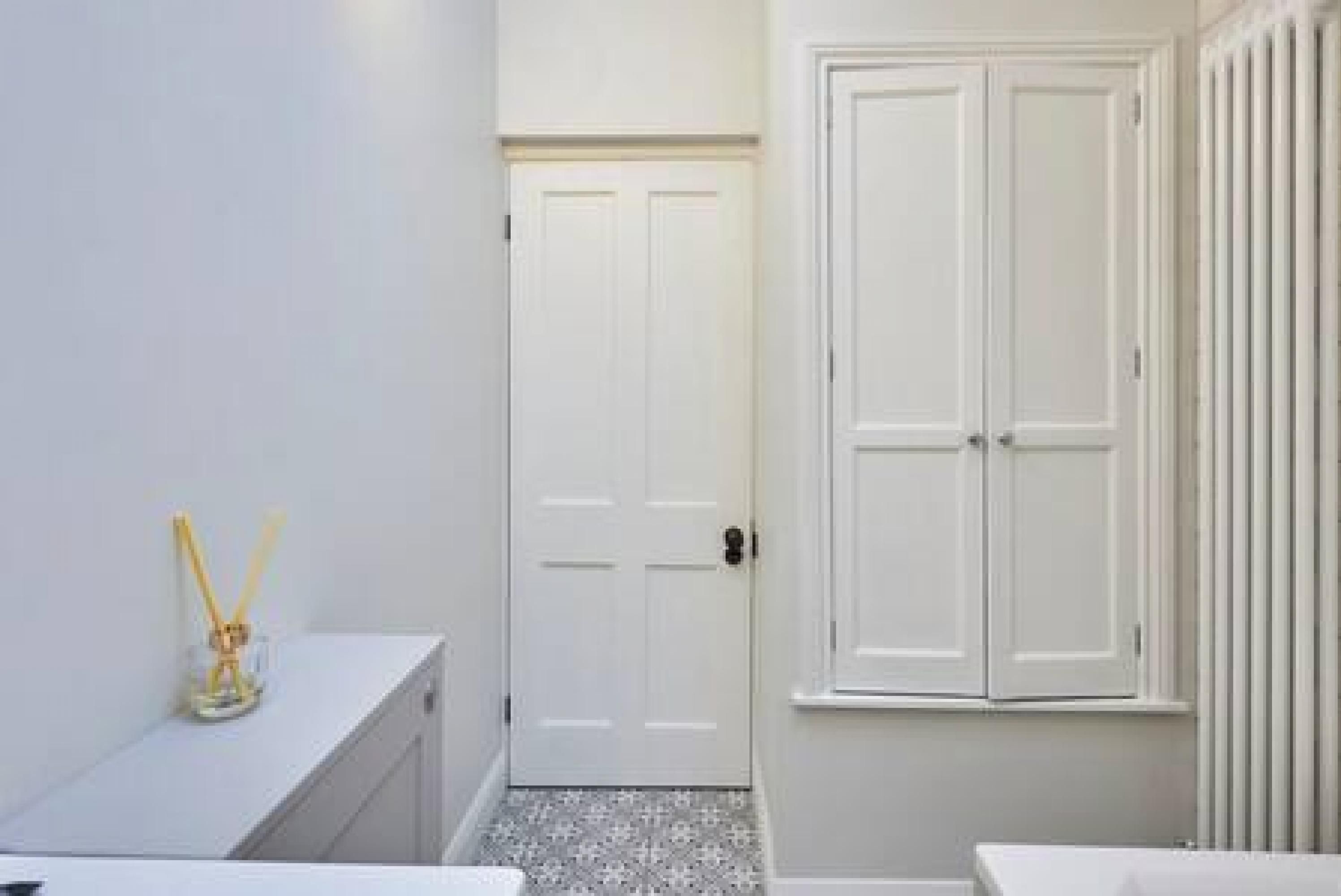 Une salle de bain avec une porte blanche, un lavabo blanc et une fenêtre avec des stores verticaux.