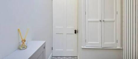 Une salle de bain avec une porte blanche, un lavabo blanc et une fenêtre avec des stores verticaux.