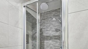A modern bathroom with a glass shower enclosure, a wall-mounted towel rack, and a textured tile backsplash. - Host Stay Millers Coach House (Hexham)