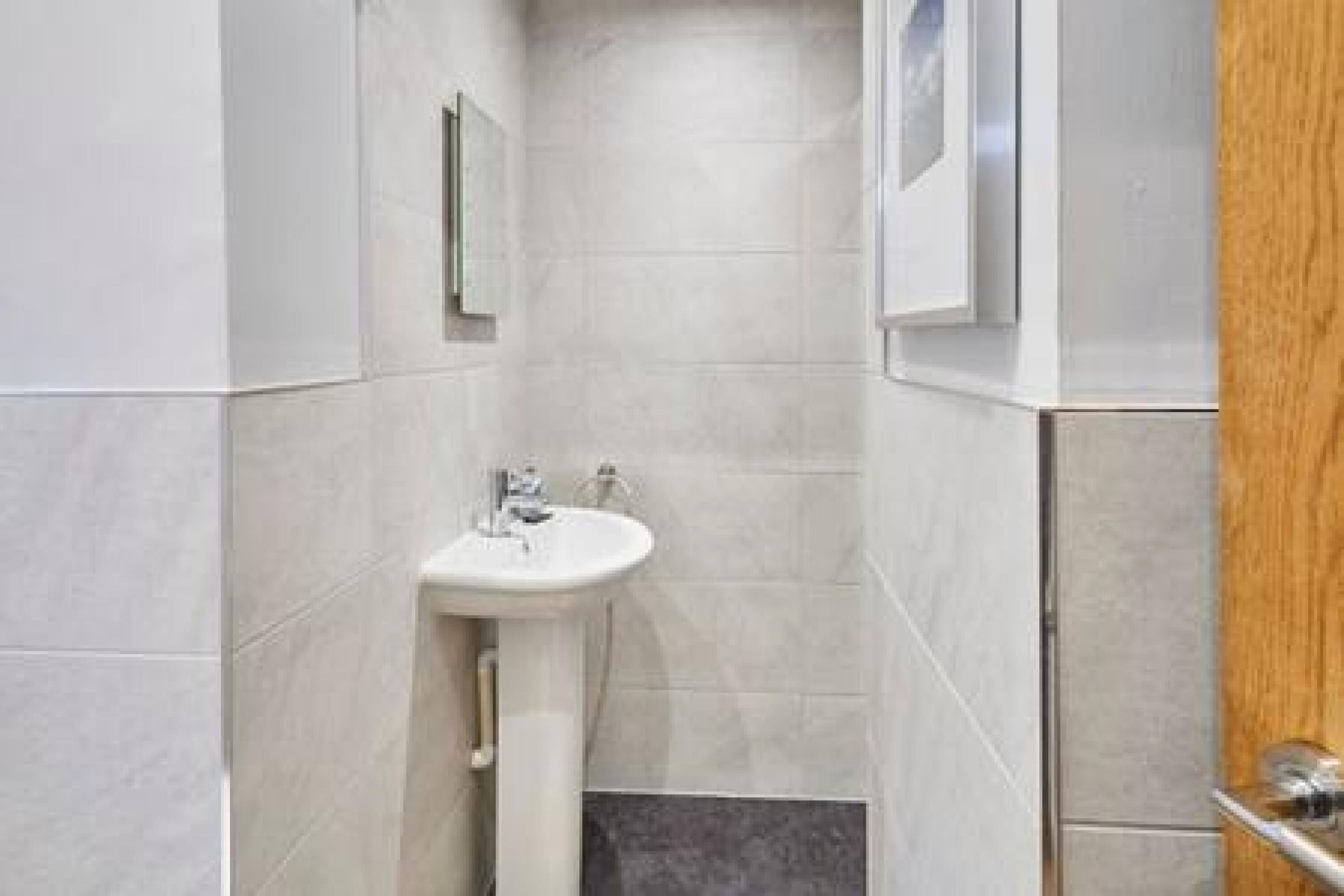 A modern bathroom with a pedestal sink, tiled walls, and a wooden door.