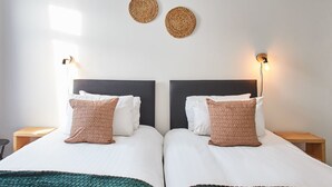 A double bed with white bedding and two brown pillows, a dark headboard, and two woven wall decorations. - Host Stay North Shore Cottage (Newbiggin-by-the-Sea)