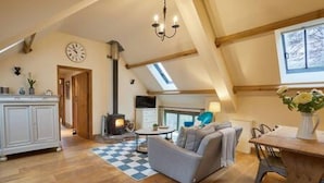 A cozy living room with a fireplace, a sofa, a dining table, and a chandelier. - Host Stay Llewenau Draw Barn (Crickhowell)