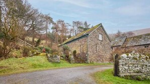 A stone building with a sloped roof, a stone wall, and a gravel path leading to it. - Host Stay Llewenau Draw Barn (Crickhowell)