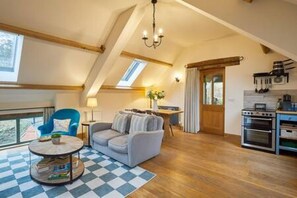 A cozy living room with a sofa, a round coffee table, and a view of the outdoors through a large window. - Host Stay Llewenau Draw Barn (Crickhowell)