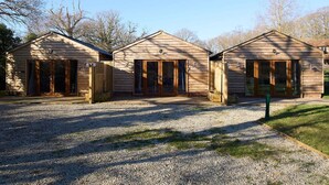 Three wooden cabins with large sliding glass doors, a gravel driveway, and a grassy area in front. - Host Stay Willow Barn (Ashford)
