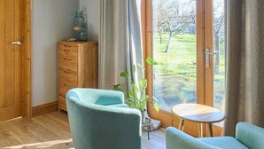 A room with a wooden wardrobe, a small table with a chair, and a view of a grassy area through a glass door. - Host Stay Orchard Barn (Ashford)