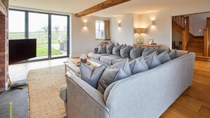 A modern living room with a sectional sofa, a flat-screen TV, and a large sliding glass door leading to a garden. - Host Stay Coed Barn (Brecon)