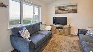 A living room with a grey sofa, a flat-screen TV, and a painting of a boat on the wall. - Host Stay Sea View Road (Bridlington)