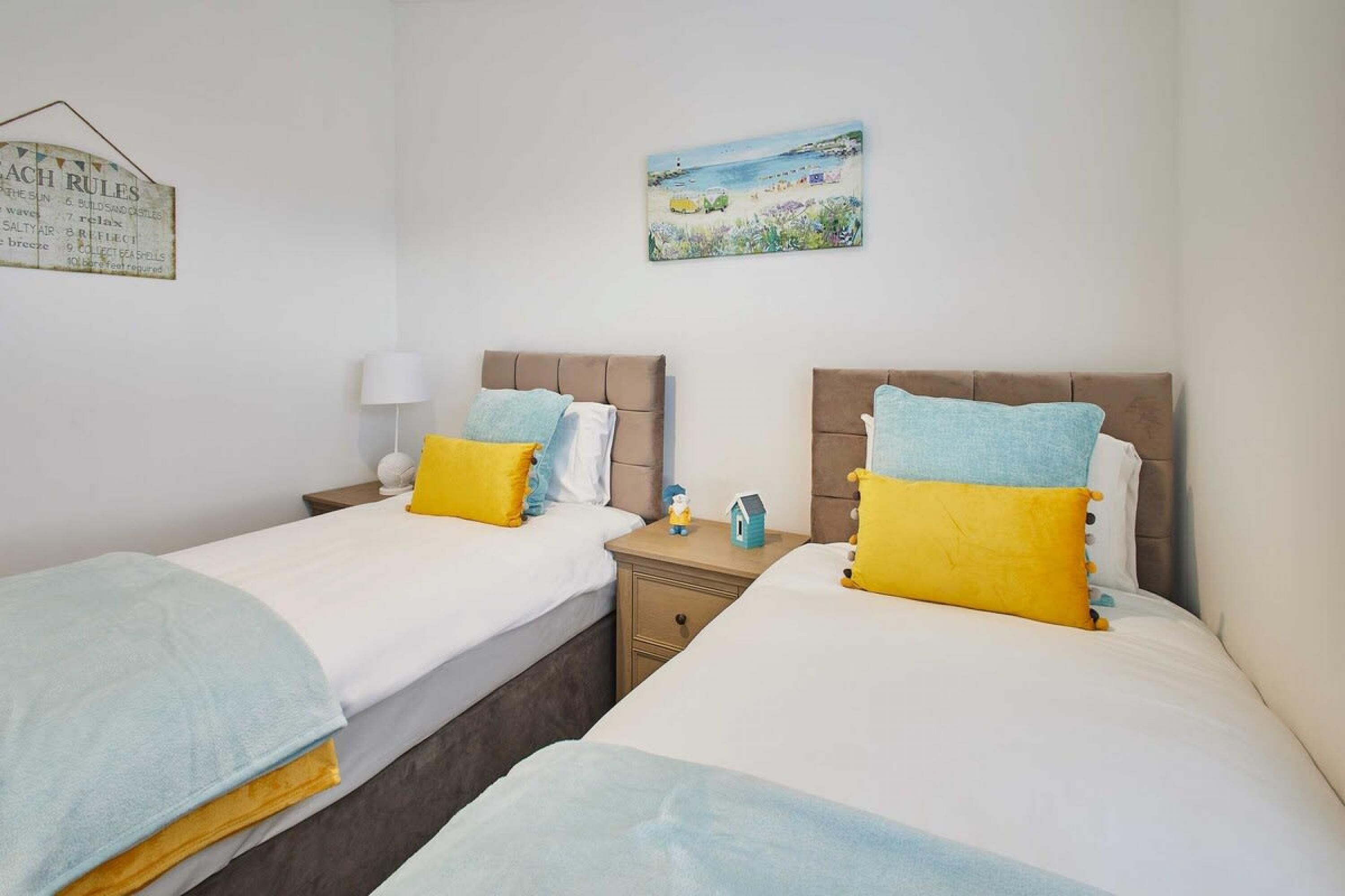 Una habitación con dos camas, cada una con cabecera, mesita de noche, lámpara y un pequeño objeto decorativo.